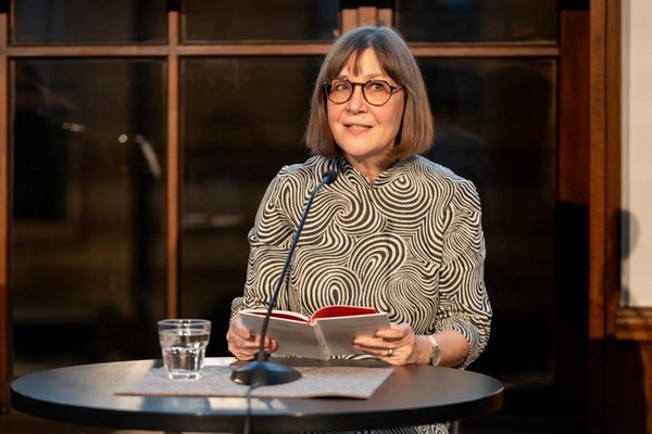 Eine Frau in einem schwarz-weiß-gemusterten Oberteil sitzt am Tisch und liest